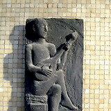 Oskar Bottoli, Dichter und Musiker, Bronzerelief (1965/66) als Hauszeichen am Gemeindebau ‚Bundesländerhof‘, Bernouilligasse 4–8, Wohnblock I: TIROL, Stiege 4 (Wien XXII). Das Relief zitiert die bekannte Darstellung aus dem Codex Manesse (s. Art. Walther von der Vogelweide [Abb.]), allerdings mit Wandervogelgitarre.